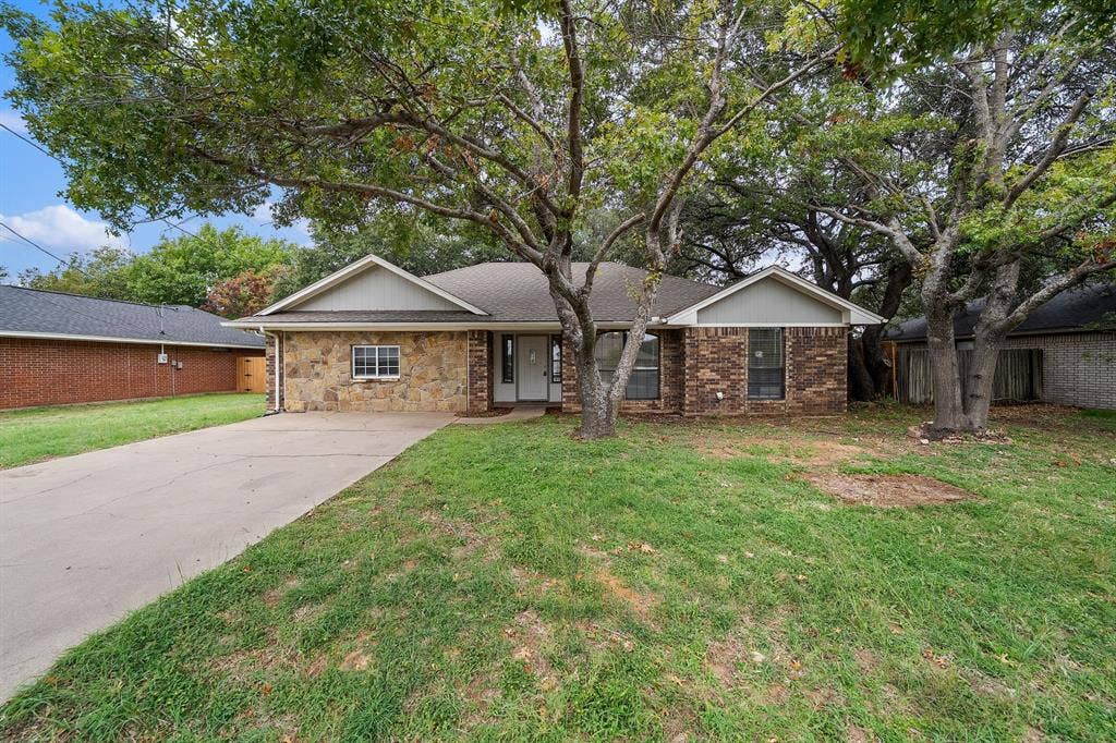 4043 Country Meadows Circle, Granbury, TX 76049 Single-story exterior featuring a stone and brick facade, gabled rooflines, concrete driveway, and mature landscaping