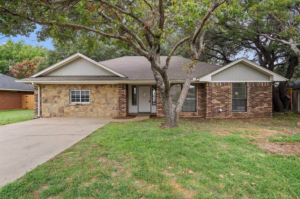 4043 Country Meadows Circle, Granbury, TX 76049 Exterior facade featuring a combination of natural stone and brick masonry, a concrete driveway, and gabled rooflines with neutral-toned siding accents