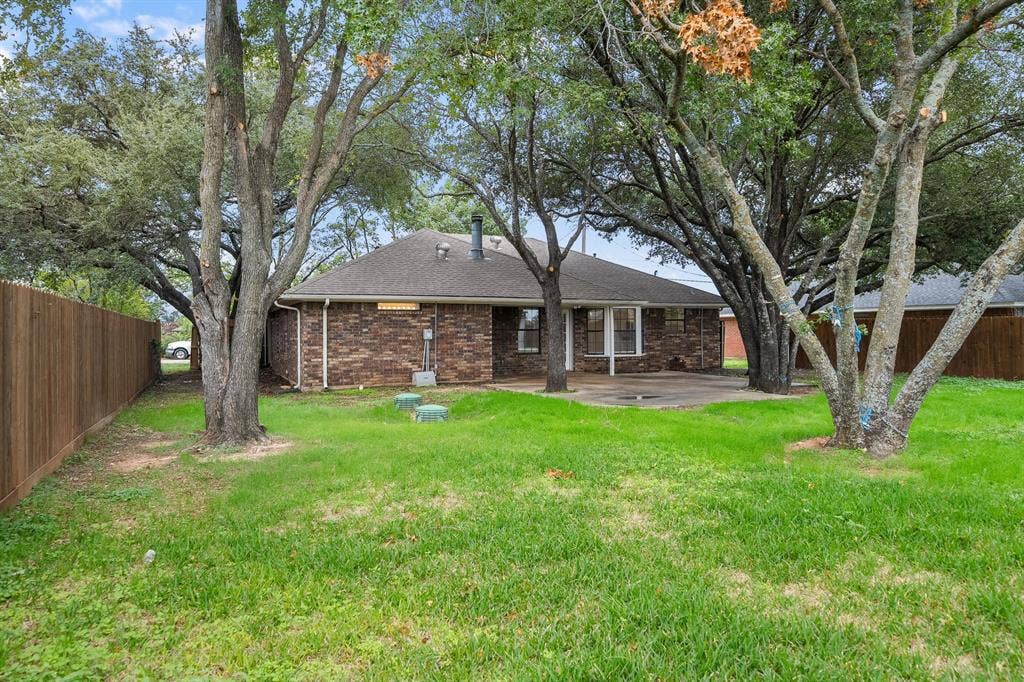 4043 Country Meadows Circle, Granbury, TX 76049 Rear exterior featuring brick siding, a concrete patio, mature trees, and a wooden privacy fence