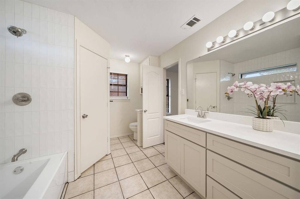 4043 Country Meadows Circle, Granbury, TX 76049 Bathroom featuring tile flooring, a white vanity with an integrated countertop, a full-width wall mirror, and a tub-shower combination with floor-to-ceiling tile surround