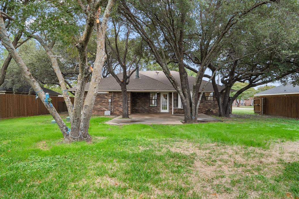 4043 Country Meadows Circle, Granbury, TX 76049 Backyard featuring a concrete patio, brick exterior, wood privacy fencing, and mature canopy trees