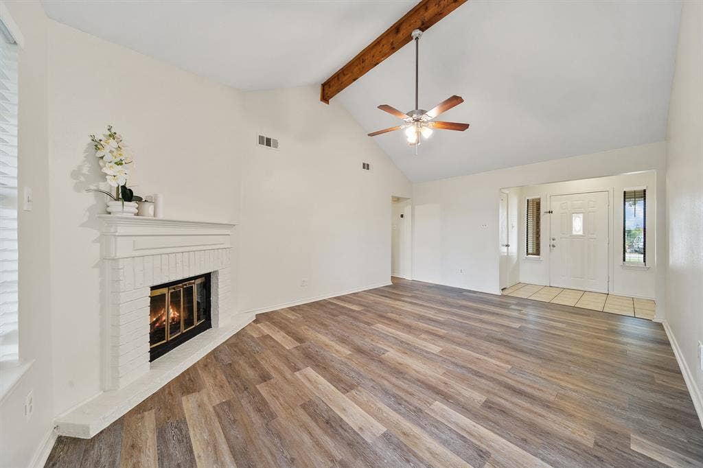 4043 Country Meadows Circle, Granbury, TX 76049 Vaulted ceiling featuring an exposed wood beam, fireplace with a painted brick surround, and wood-finish flooring