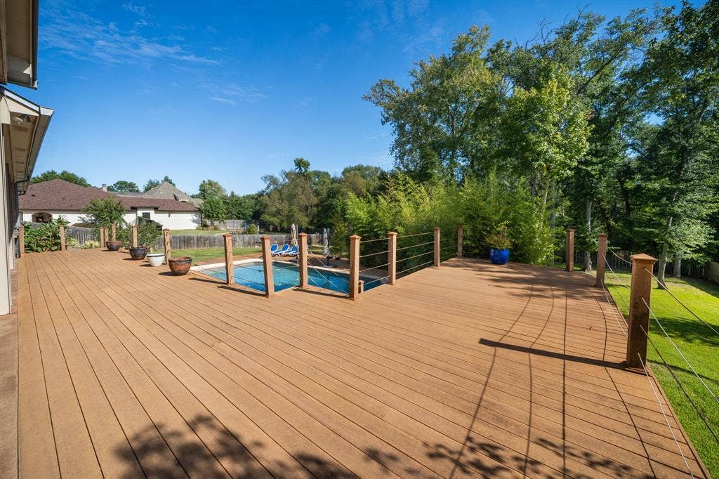 1997 Hollystone Drive, Tyler, TX 75703 Expansive wood-finish deck featuring a sunken in-ground swimming pool, horizontal cable railing system, and mature tree-lined perimeter