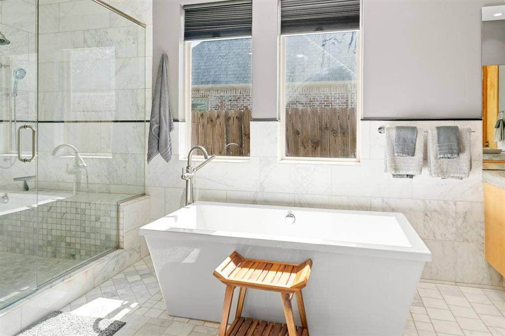 1997 Hollystone Drive, Tyler, TX 75703 Freestanding soaking tub with chrome fixtures, glass-enclosed shower, stone wall tile, and light-toned floor tile