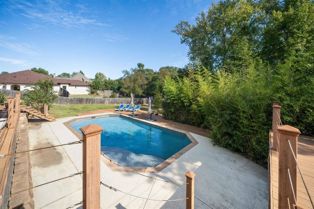 1997 Hollystone Drive, Tyler, TX 75703 In-ground swimming pool with concrete decking, surrounded by mature trees and wood-finish railings with cable tension detailing