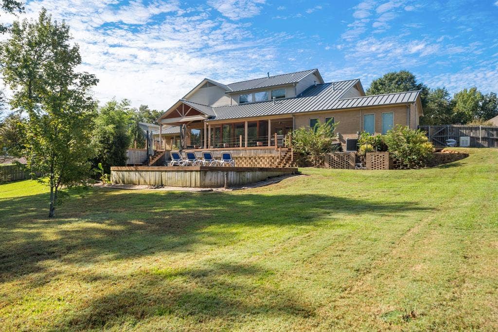1997 Hollystone Drive, Tyler, TX 75703 Multi-level residence featuring a metal roof, expansive wood deck, and masonry exterior walls, situated on a large lot with mature landscaping