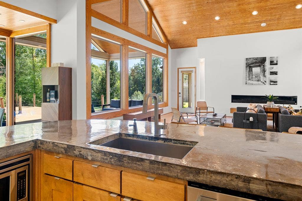 1997 Hollystone Drive, Tyler, TX 75703 Kitchen featuring a stone countertop, an undermount sink with a gooseneck faucet, custom wood cabinetry, a vaulted wood-paneled ceiling, and expansive floor-to-ceiling windows