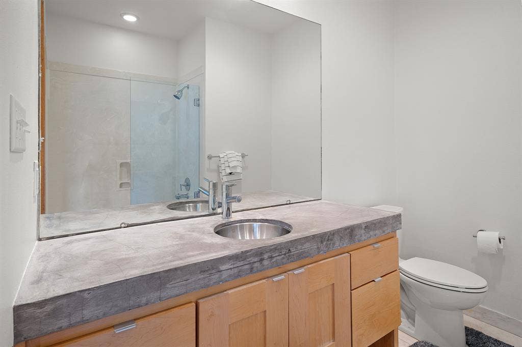 1997 Hollystone Drive, Tyler, TX 75703 Bathroom featuring a concrete-style countertop, light wood cabinetry, a large wall-mounted mirror, an undermount circular sink with a chrome faucet, and a shower with a glass enclosure