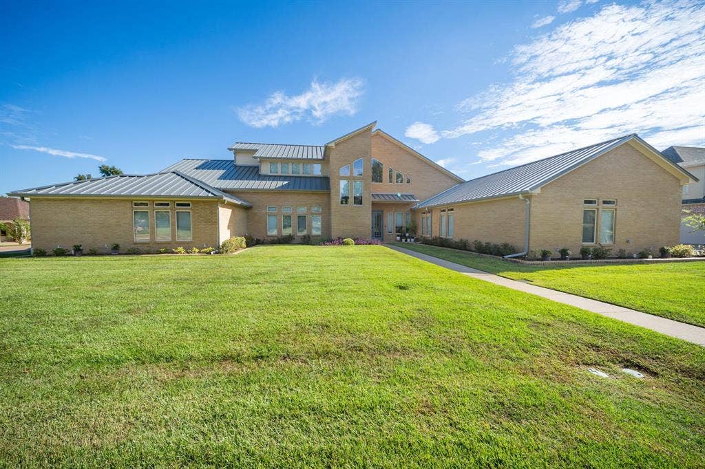 1997 Hollystone Drive, Tyler, TX 75703 Contemporary exterior featuring a light-toned brick facade, standing seam metal roof, multi-level architectural design, and geometric windows set within an expansive grass lawn