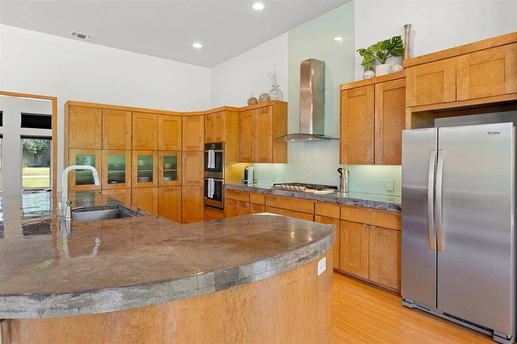 1997 Hollystone Drive, Tyler, TX 75703 Kitchen featuring wood cabinetry, concrete countertops, stainless steel built-in double ovens, stainless steel range hood, and wood-finish flooring