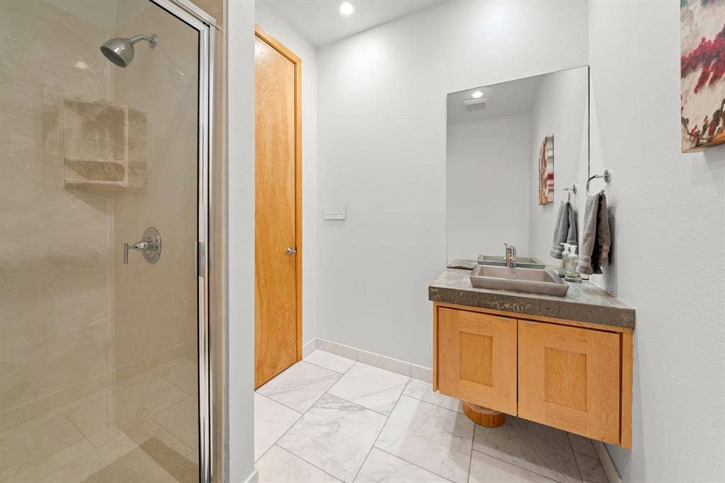 1997 Hollystone Drive, Tyler, TX 75703 Bathroom featuring a shower with a glass enclosure, wall-mounted wood vanity, rectangular vessel sink, concrete-finish countertop, and large-format tile flooring