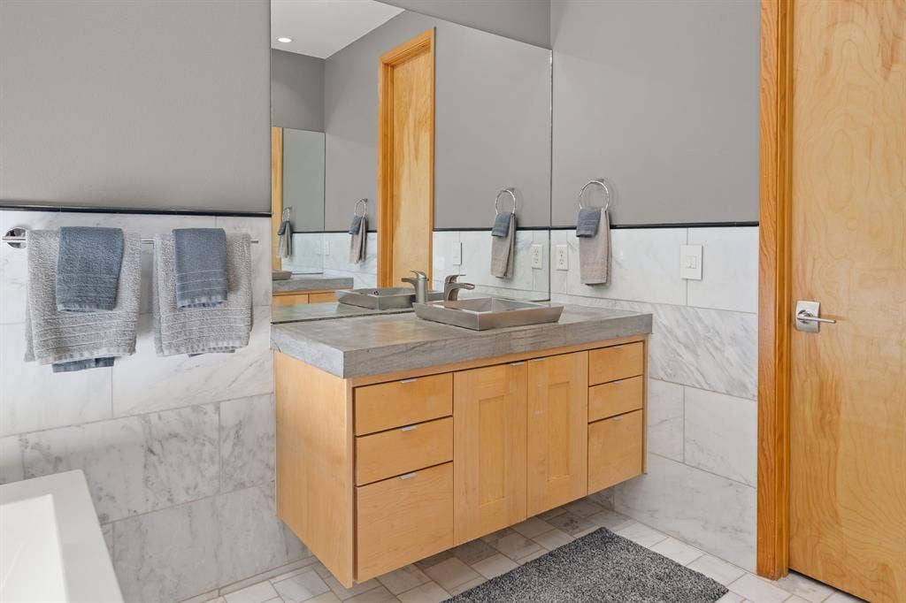 1997 Hollystone Drive, Tyler, TX 75703 Floating light wood vanity featuring a concrete-style countertop, integrated vessel sink, polished metal hardware, and large-format wall tiling