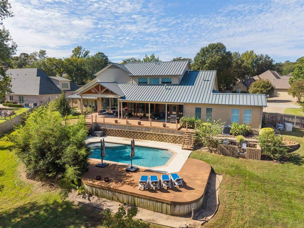 1997 Hollystone Drive, Tyler, TX 75703 Multi-level exterior featuring a standing-seam metal roof, expansive elevated wood deck, inground swimming pool with concrete surround, and structured retaining walls