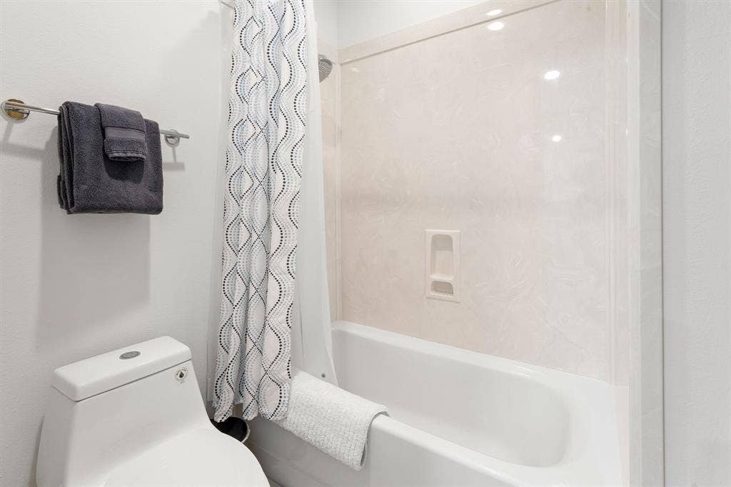 1997 Hollystone Drive, Tyler, TX 75703 Full-height tub and shower surround with integrated storage niche, one-piece dual-flush toilet, and wall-mounted metal towel rack