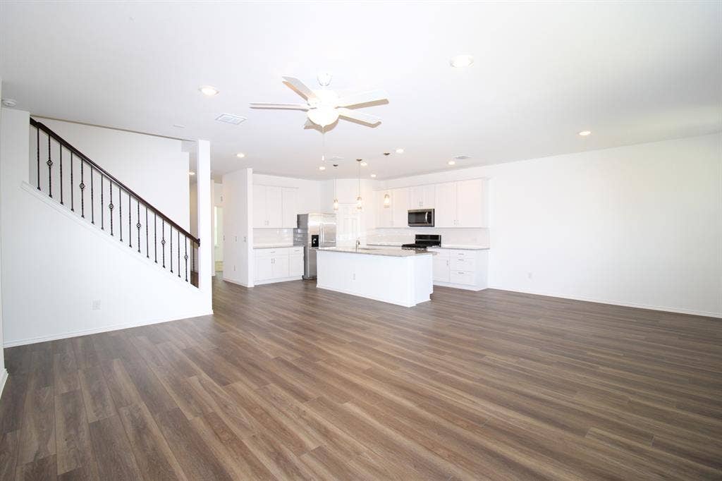 Open-concept interior featuring wood-finish flooring, white cabinetry, a center island with stone-finish countertop, recessed lighting, and a staircase with metal balusters