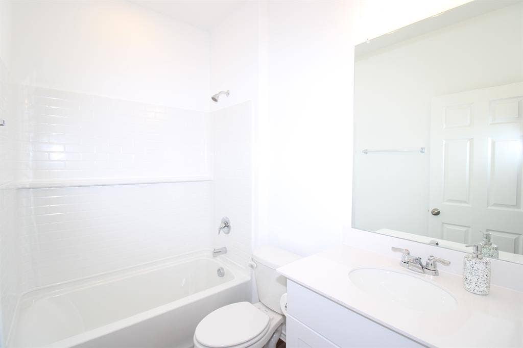 Bathroom featuring a white vanity with a solid-surface countertop, an oval undermount sink, a full-width vanity mirror, and a bathtub with white subway-style wall tiling