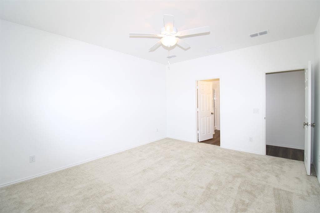 Room featuring neutral wall-to-wall carpeting, white walls, a ceiling fan with integrated light fixture, and two interior doors