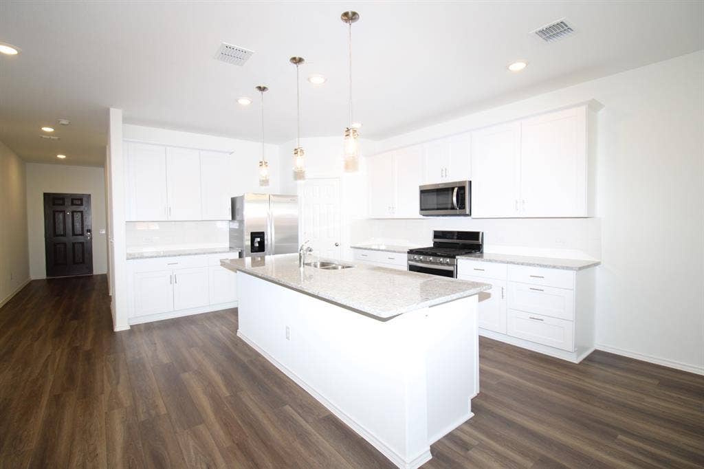 Kitchen featuring a stone-look countertop island, white shaker-style cabinetry, wood-finish flooring, stainless steel appliances, and multi-pendant lighting