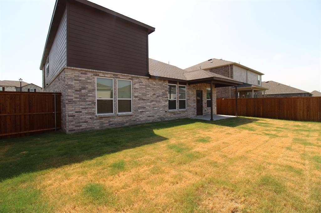 Exterior featuring mixed-material brick and horizontal siding, covered rear patio, and a fully fenced backyard