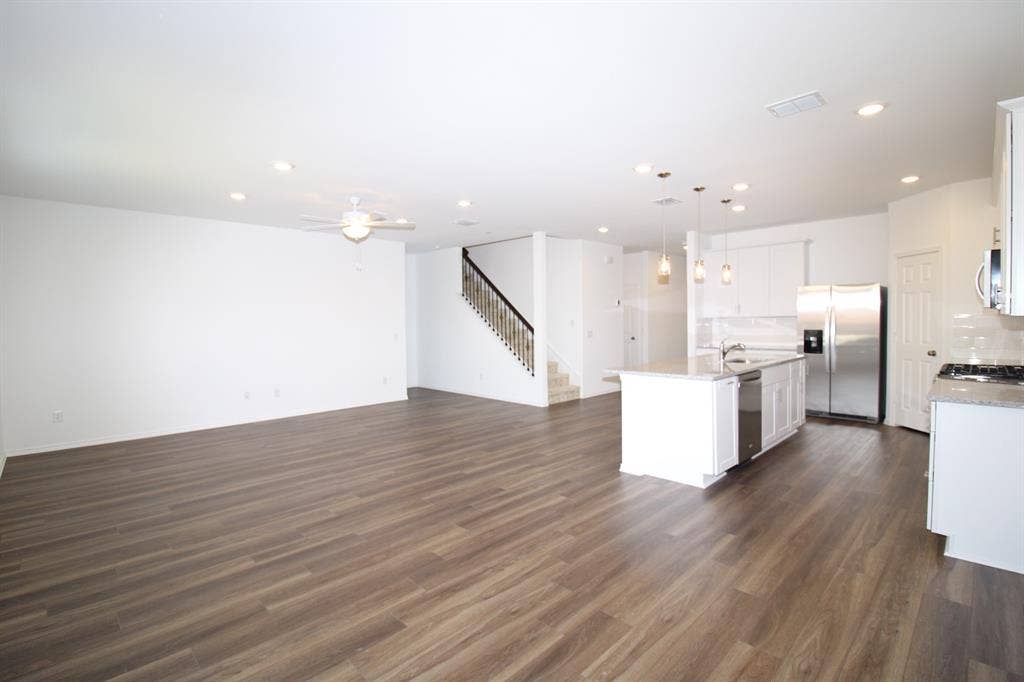 Open-concept interior featuring wood-finish flooring, recessed lighting, a center kitchen island with stone-surface countertops, stainless steel appliances, and a staircase with a dark-finish banister