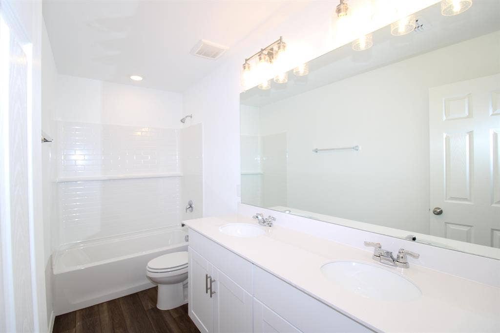 Dual-sink vanity with a solid-surface countertop, white shaker-style cabinetry, full-width mirror, and subway tile tub surround