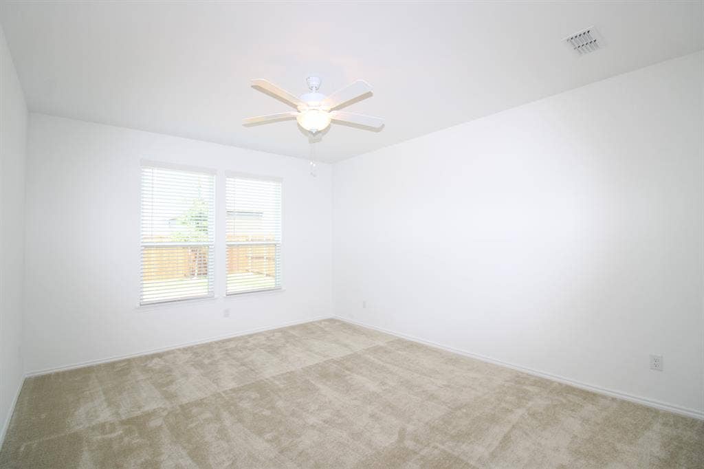 Neutral-toned wall-to-wall carpeting, dual windows with horizontal blinds, and a white ceiling fan with integrated lighting