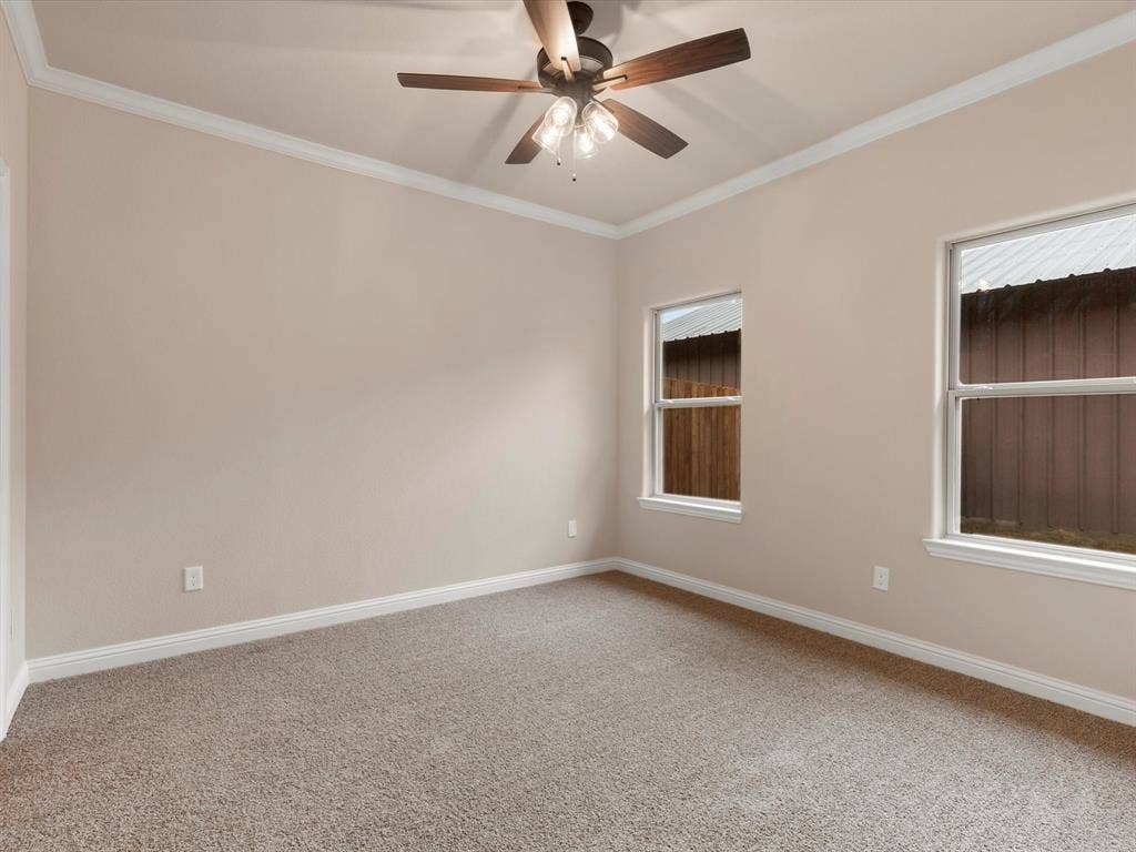 Neutral-toned interior featuring wall-to-wall carpeting, crown molding, double-hung windows, and a central ceiling fan with multi-light fixture