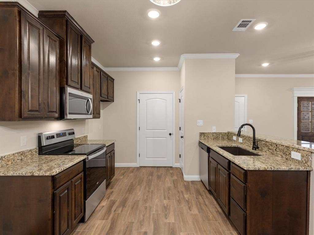 Kitchen featuring dark wood-finish cabinetry, stone-finish countertops, stainless steel appliances, a black gooseneck faucet, and wood-finish flooring