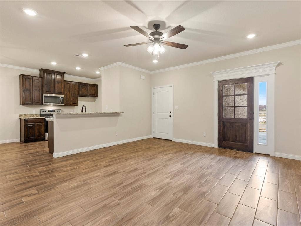 Open-concept interior featuring wood-finish flooring, recessed lighting, stained wood cabinetry, stone countertops, and a glass-paneled entry door with sidelight