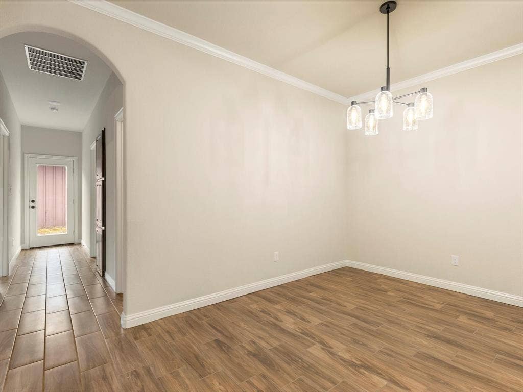 Room featuring an arched entryway, wood-finish tile flooring, crown molding, and a five-light tiered chandelier with glass shades