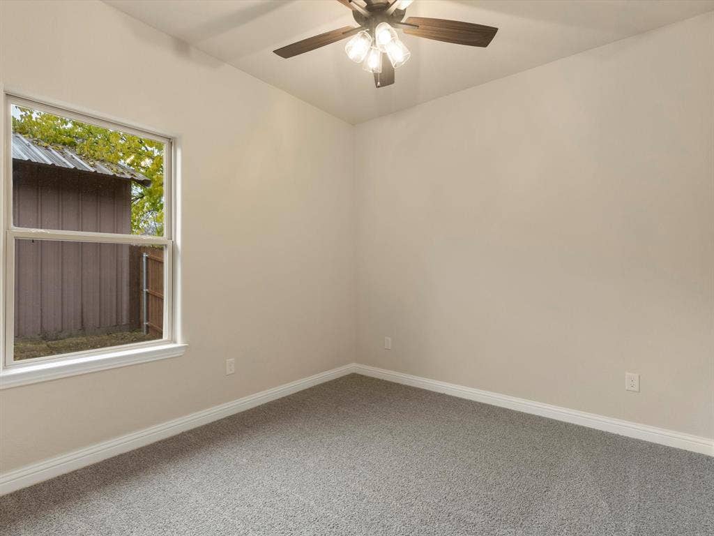 Neutral-toned interior featuring wall-to-wall carpeting, a multi-light ceiling fan, and a single-hung window with a view of the exterior grounds