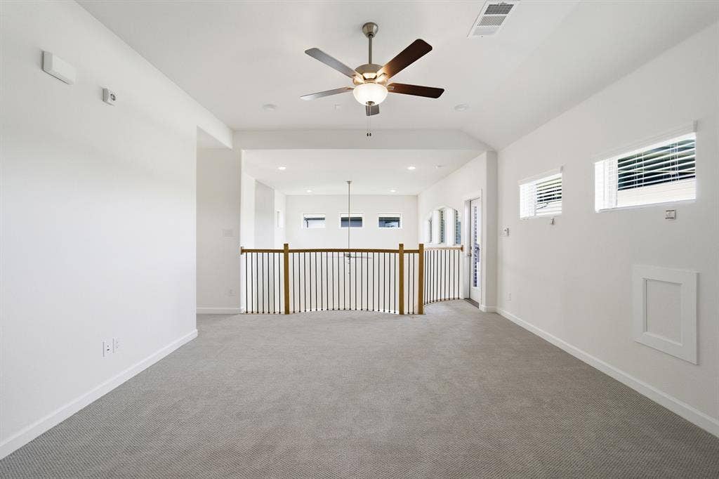 Carpeted loft area featuring a ceiling fan, multiple windows with blinds, and a white framed access panel