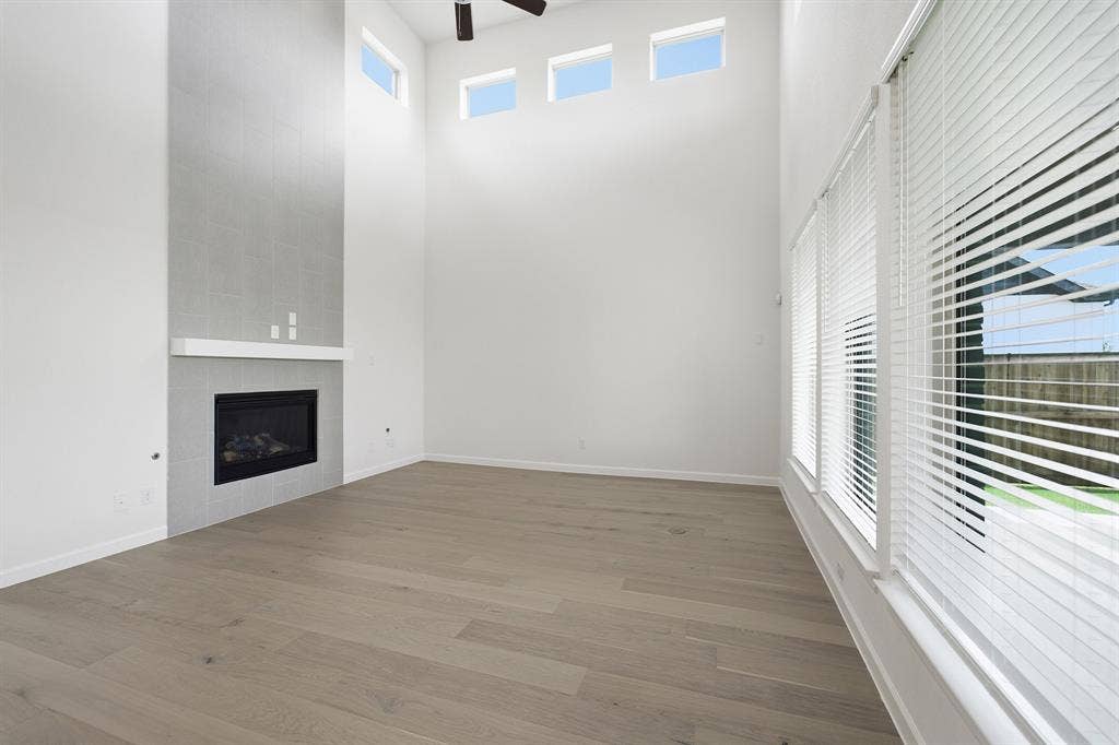 Vaulted ceiling living space featuring wood-finish flooring, a contemporary fireplace with a white mantel, and a tiled accent wall