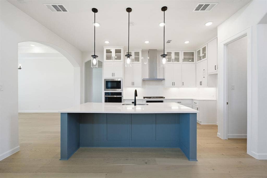 Modern kitchen featuring a blue-paneled island with a white countertop and three pendant lights