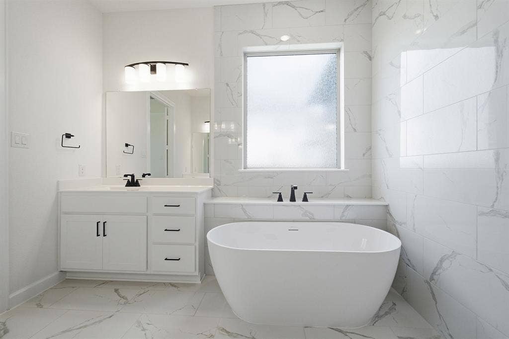 Modern bathroom featuring a freestanding soaking tub with matte black fixtures, a single vanity with white cabinetry, a rectangular undermount sink, and a framed mirror