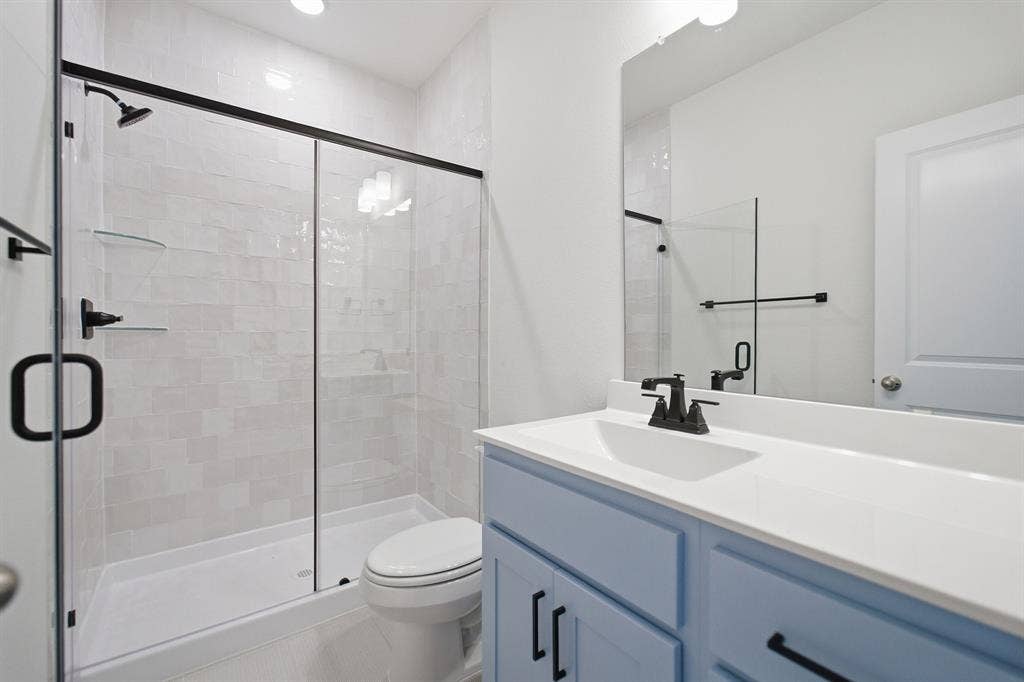 Modern bathroom featuring a walk-in shower with a glass enclosure, light-toned tile surround, and matte black fixtures