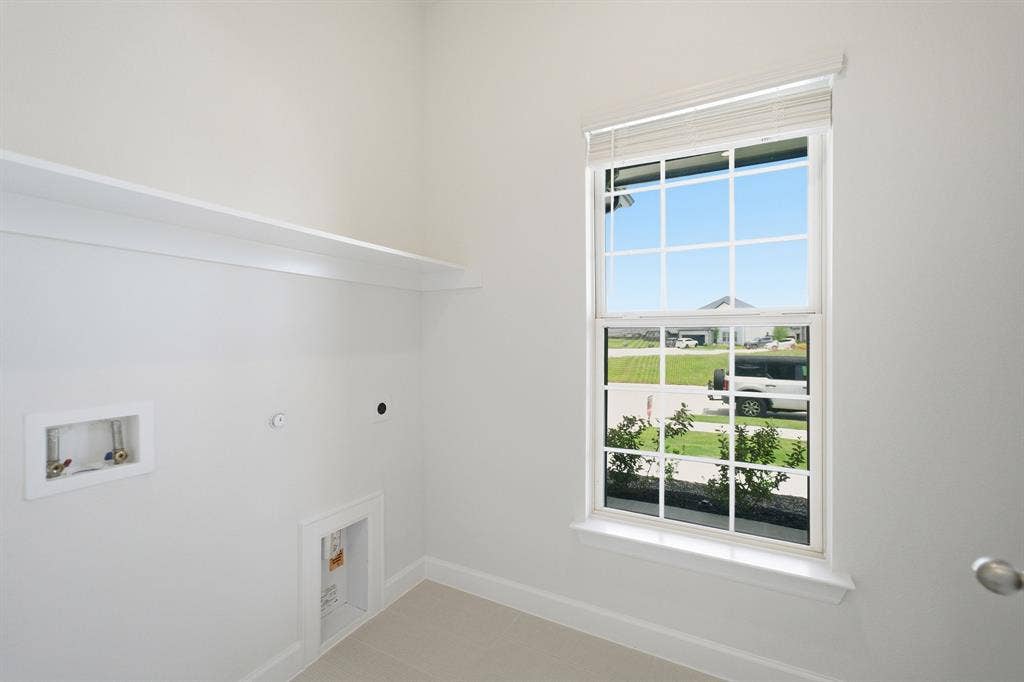 Utility room featuring a single-pane window with blinds, a built-in wall shelf, and light-colored flooring
