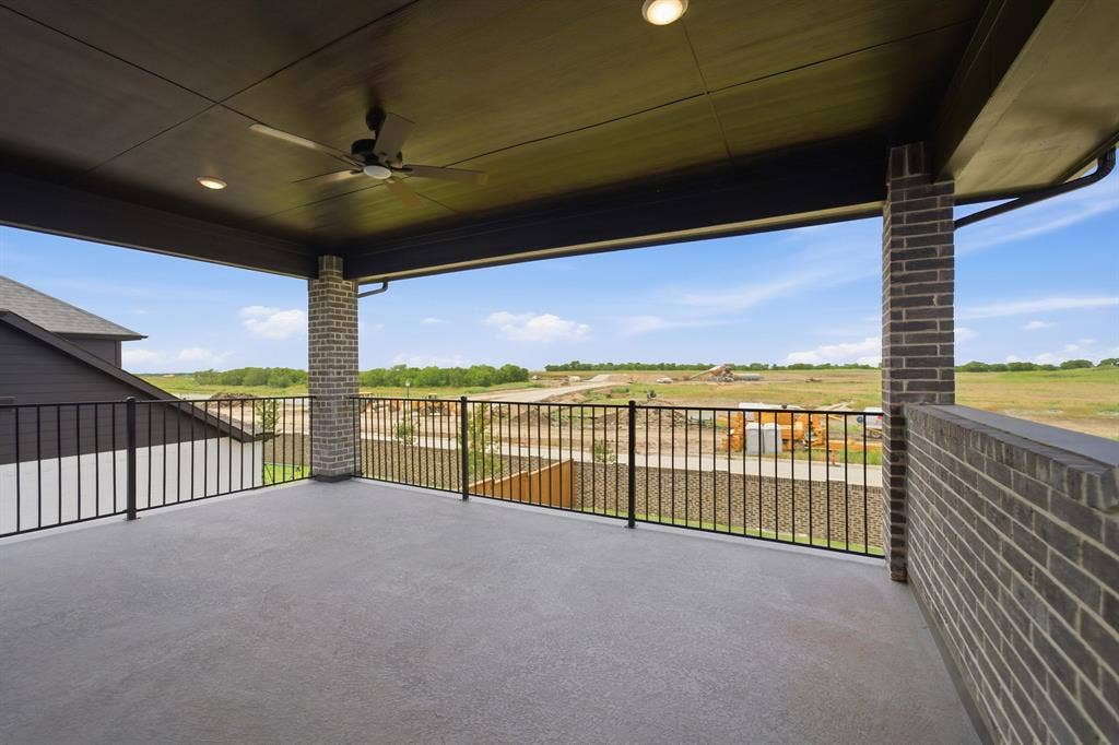 Expansive covered patio featuring a dark brick privacy wall, wrought iron railing, ceiling fan, and recessed lighting