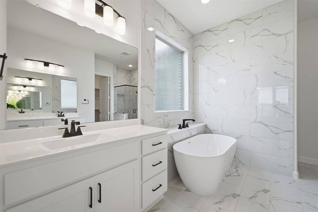 Modern bathroom featuring a freestanding tub, white marble-look wall tiling, and dual vanities with quartz countertops