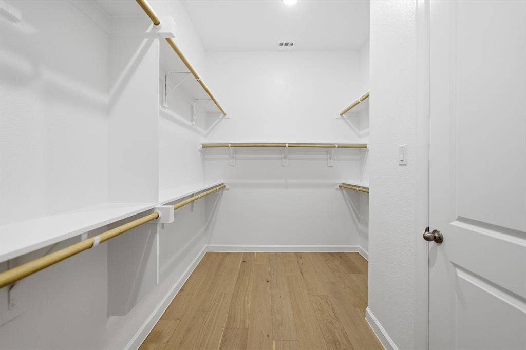 Spacious walk-in closet featuring wood-finish flooring, ample white shelving, multiple hanging rods, and recessed lighting