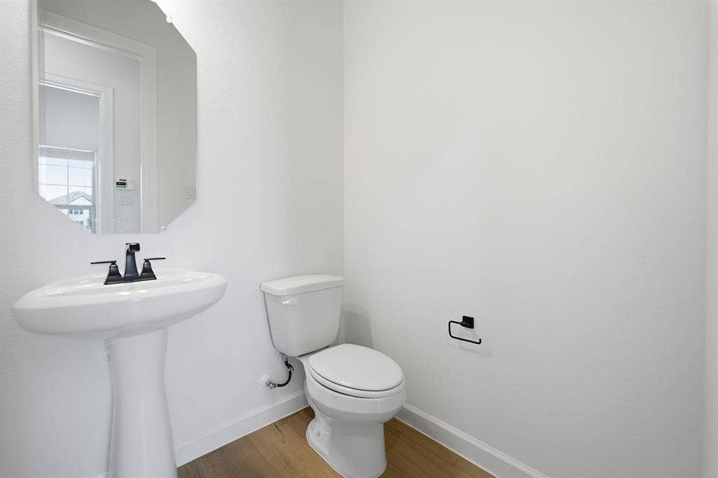 Pedestal sink with matte black faucet, elongated toilet, and wood-finish flooring