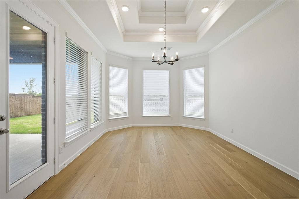 Spacious room featuring wood-finish flooring, a tray ceiling with recessed lighting, an iron chandelier, a bay window with blinds, and a glass-paneled exterior door