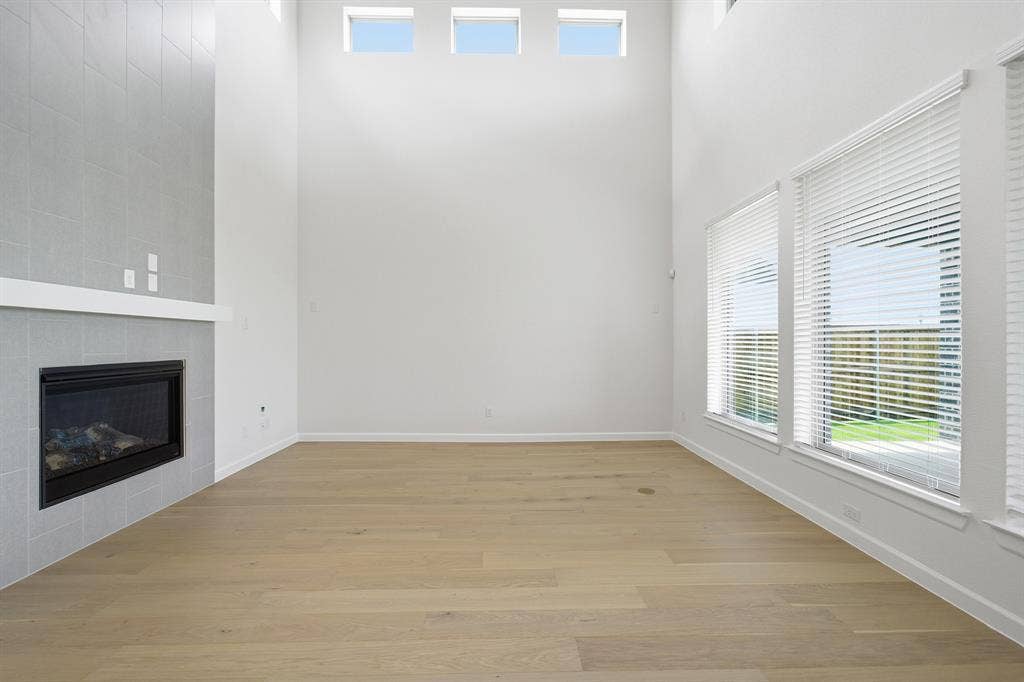 Two-story living area featuring a tiled fireplace with mantel, wood-finish flooring, and multiple windows with blinds