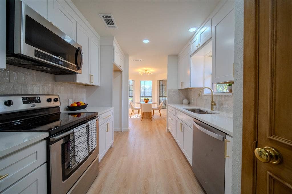 2213 Moore Drive, Plano, TX 75074 Kitchen featuring white shaker-style cabinetry, stainless steel appliances, light-toned stone countertops, a textured backsplash, and light wood-finish flooring