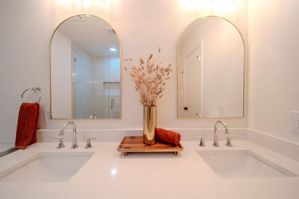 2213 Moore Drive, Plano, TX 75074 Dual vanity featuring stone-finish countertops, undermount sinks, arched mirrors with gold-tone frames, and three-handle faucets