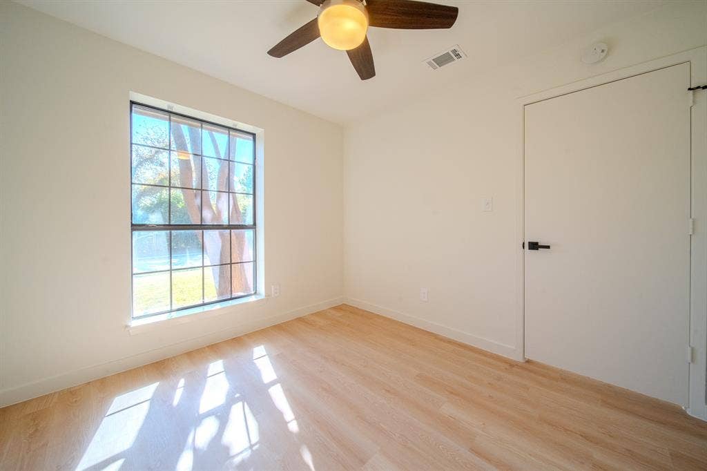 2213 Moore Drive, Plano, TX 75074 Wood-finish flooring, grid-pattern window, ceiling fan with integrated lighting, and a flush-panel interior door with matte black hardware