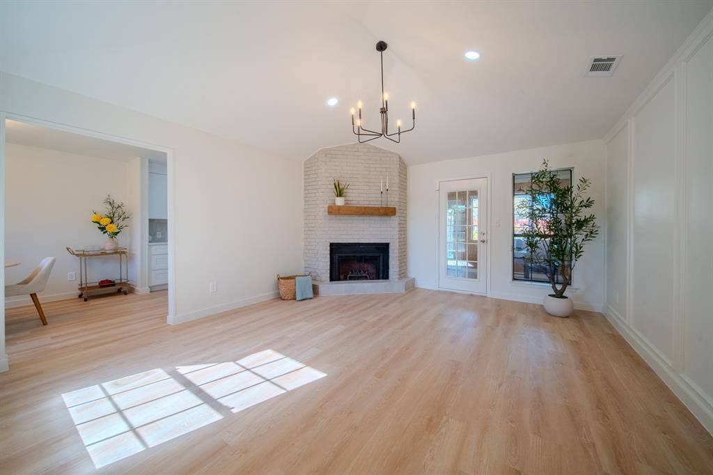 2213 Moore Drive, Plano, TX 75074 Open living area featuring light-toned wood-finish flooring, a corner brick fireplace with a natural wood mantel, recessed lighting, a modern multi-arm chandelier, and decorative wall molding
