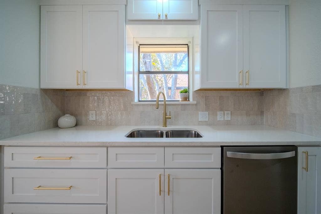 2213 Moore Drive, Plano, TX 75074 Shaker-style cabinetry with brass hardware, solid surface countertops, metallic finish faucet, stainless steel dishwasher, and textured tile backsplash