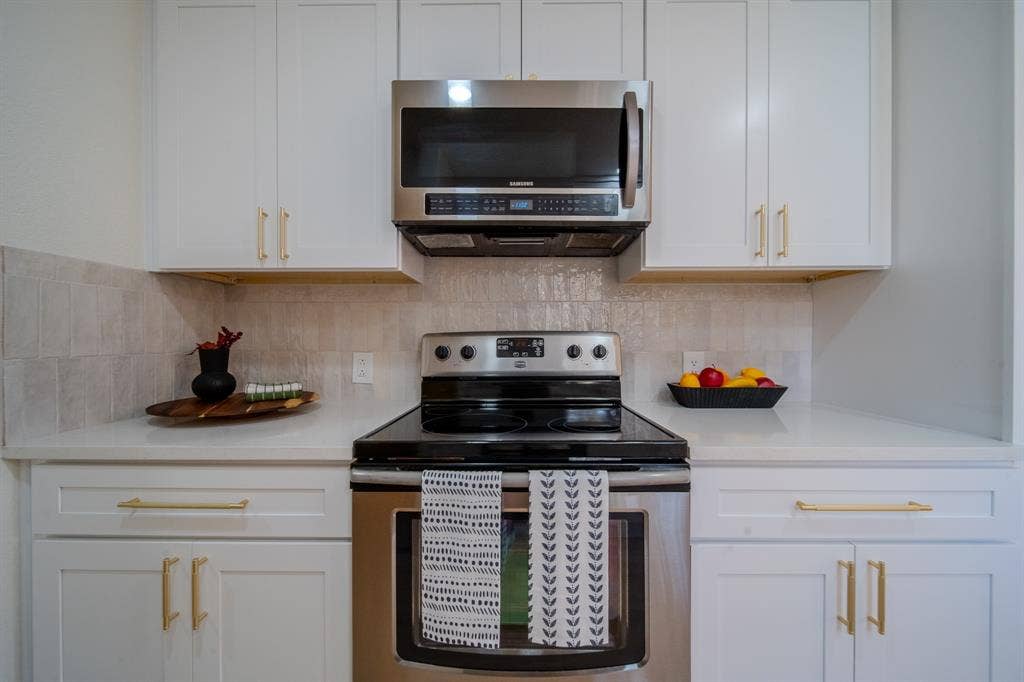 2213 Moore Drive, Plano, TX 75074 White shaker-style cabinetry with gold-tone hardware, stainless steel microwave, glass cooktop range, solid-surface countertops, and textured tile backsplash