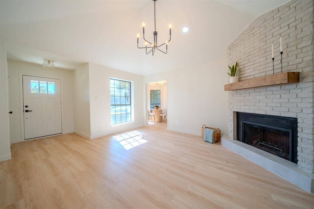 2213 Moore Drive, Plano, TX 75074 Living area featuring a vaulted ceiling, wood-finish flooring, and a fireplace with a light-colored brick surround and natural wood mantel